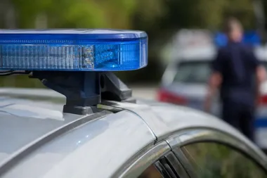 Niebieski sygnalizator świetlny na dachu policyjnego radiowozu, w tle rozmyty drugi pojazd i funkcjonariusz.