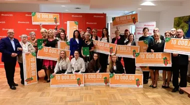 Grupa osób pozuje z dużymi czekami na tle czerwonych ścianek z logo Mazowsze podczas uroczystego wręczania nagród lub dotacji.